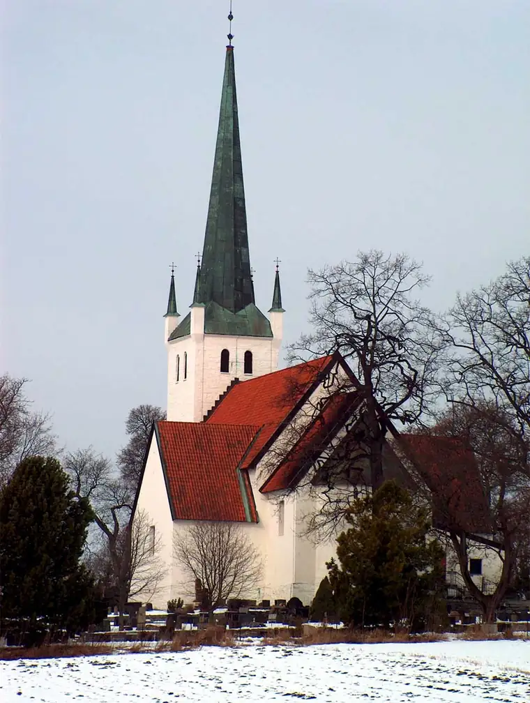 White Norderhov Church with red roofs, a tall green steeple, and gravestones in front.